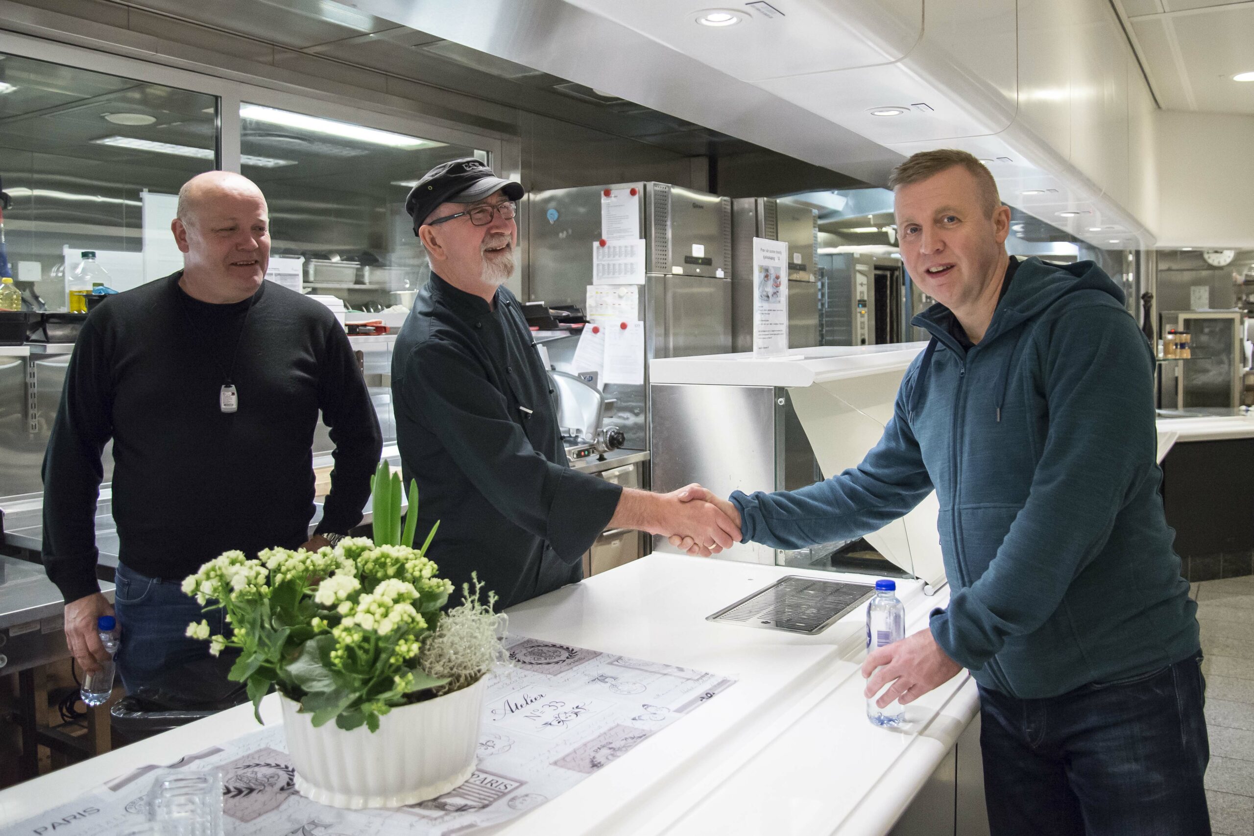 Frode Alfheim (th) gratulerer kokk Bjørn Turøy med 42 år som offshorearbeider. Bak står Per Holstein som er klubbleder i ESS. Foto: Atle Espen Helgesen